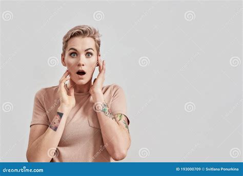 Omg Portrait Of Amazed Tattooed Woman With Pierced Nose And Short Hair In Beige T Shirt Looking