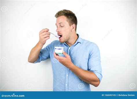 Young Handsome Man Eats Yogurt Holding Spoon Near His Mouth On Isolated