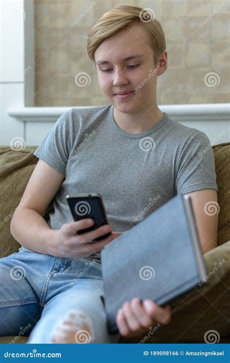 Happy Young Handsome Blond Teenage Boy Holding Book While Using Phone