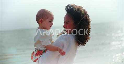 أم عربية خليجية سعودية تحمل إبنتها بحب وحنان، أم تلعب مع إبنتها بإيماءات وجه ويدين مختلفة تدل