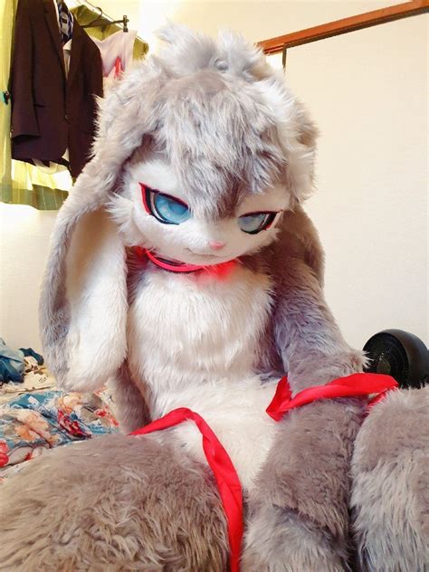 a stuffed rabbit sitting on top of a bed next to a red ribbon around it s neck