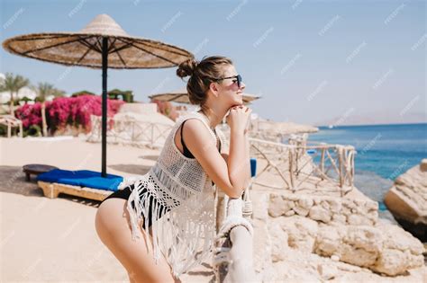 Изящная стройная девушка в купальнике и вязаной мантии стоит на пляже