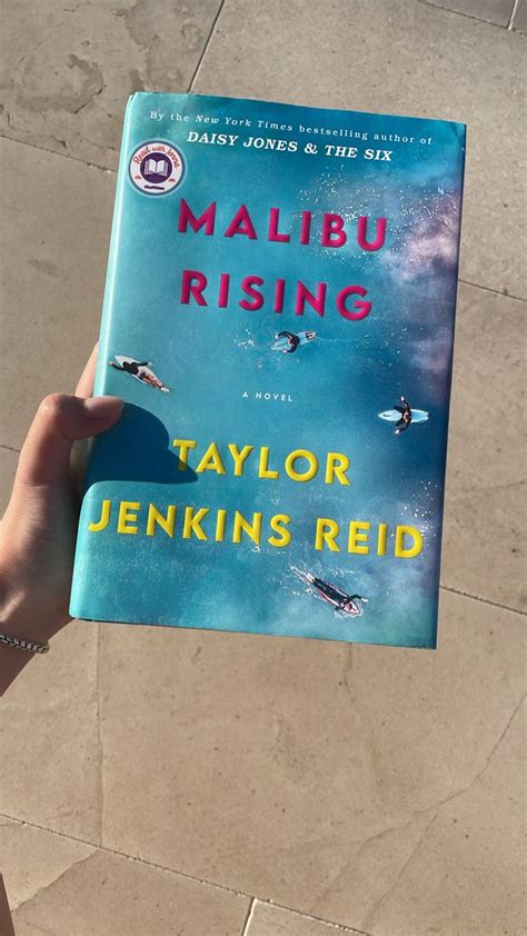 A Person Holding Up A Book About Malbu Rising In Front Of A Tiled Floor