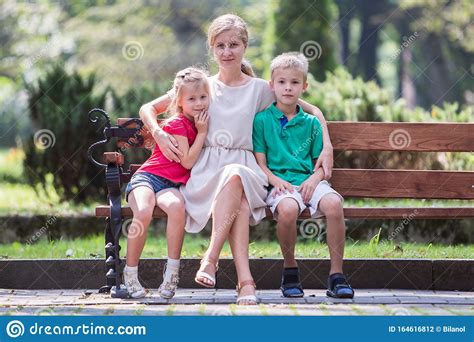 Молодая мать и двое детей весело проводят время вместе на скамейке в летнем парке Стоковое Фото
