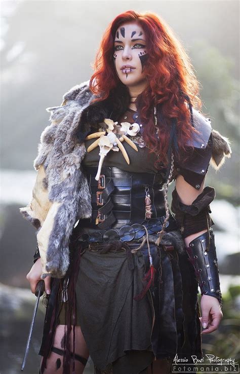 A Woman With Red Hair And Makeup Is Dressed Up As A Warrior Holding