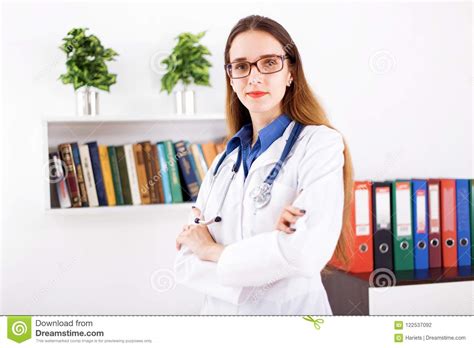 Docteur De Jeune Femme Dans Le Manteau Blanc Se Tenant Dans Le Bureau