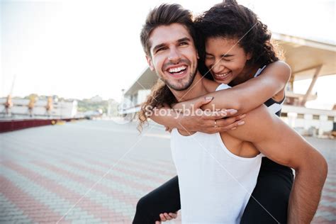 Smiling Young Man Carrying Woman On His Back And Laughing Outdoors