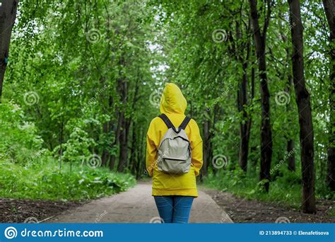 Shot Back A Young Woman In A Yellow Hoodie Stands On A Footpath In A Green Forest Stock Image