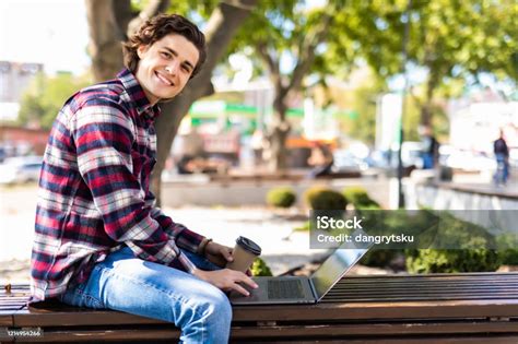 mutlu adam bankta oturuyor ve parkta dizüstü bilgisayar kullanıyor parktaki bankta dizüstü