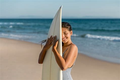 Mujer Joven Abrazando La Tabla De Surf En La Orilla Del Mar Foto Gratis