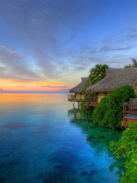 Download A Tropical Island With Thatched Huts And A Sunset Wallpaper