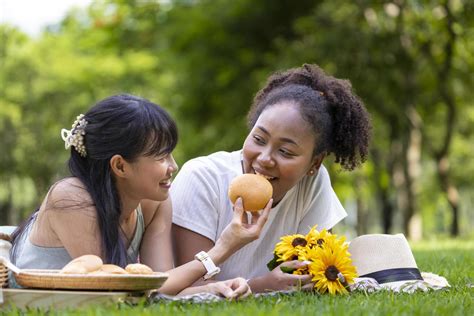 couple of lesbian people having picnic in the park during summer while having snack and lying