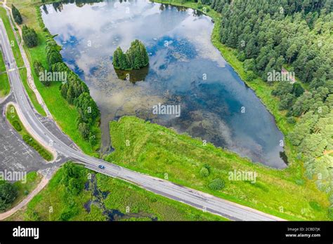 Aerial View Of Small Pond Between Green Forest And Country Road Drone