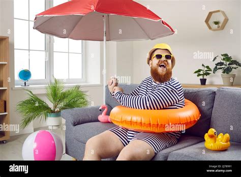 Funny Chubby Man Having Fun Sitting On Sofa In Living Room With Inflatable Swimming Circle Stock