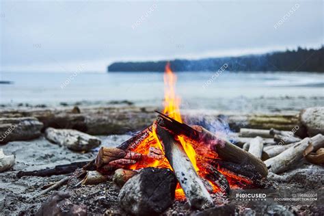 A Fire On The Beach With The Ocean And Coastline In The Background