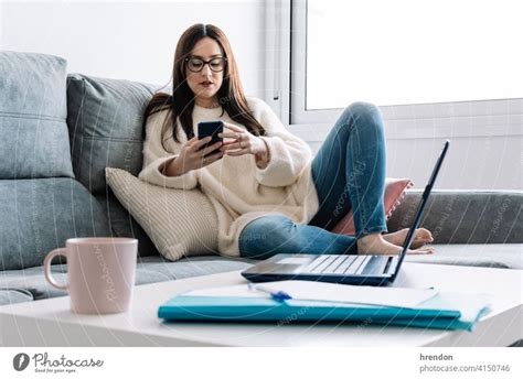 Woman Talking With Mobile Phone While Working With Laptop Sitting On A Couch At Home A Royalty