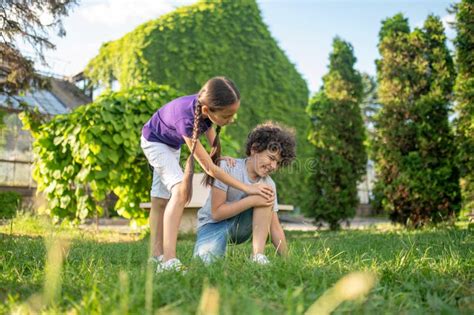 Girl Bending Over To Boy Sitting On Grass Stock Image Image Of Injury
