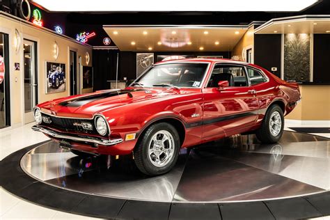 A person enjoying a drive in a 1970 Ford Maverick on a scenic road.